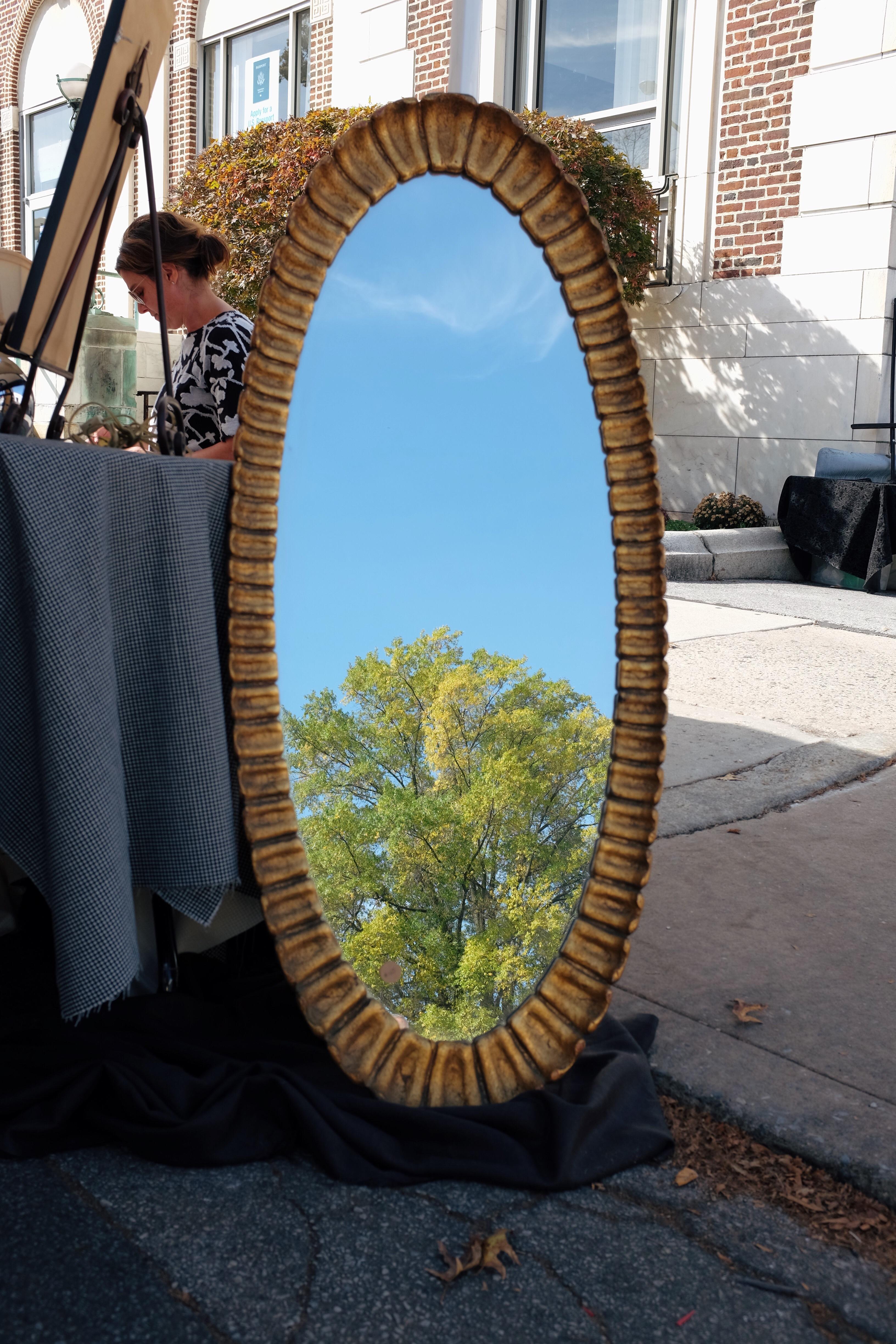 Oval mirror with an ornate metal frame, reflecting a sky and a tree