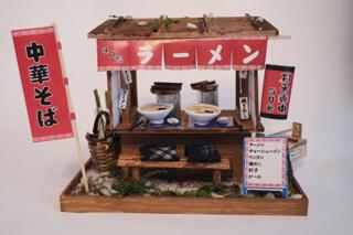 Scale model of a ramen stand with two place settings and colorful signage.