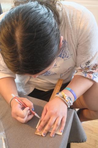 A young woman measures a piece of balsa wood.