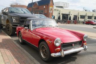 A red convertible in the foreground dwarfed by a large pickup truck behind it.