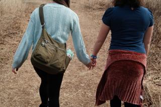 Two girls hold hands while walking.