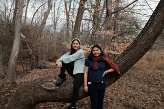Two girls pose in front of a tree trunk.