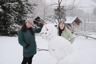 Two young women pose with a snowman.