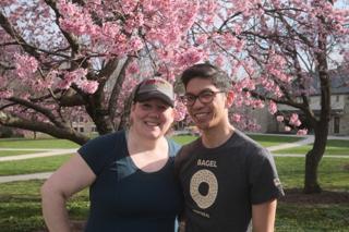 A woman and man pose in front of a cherry blossom tree.
