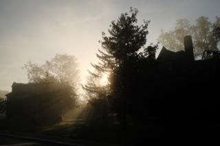 Light rays breaking through a silhoutted house and tree.