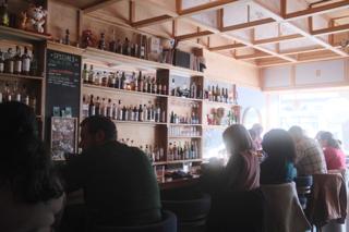 Patrons at a bar, backlit by late afternoon sun through the windows.