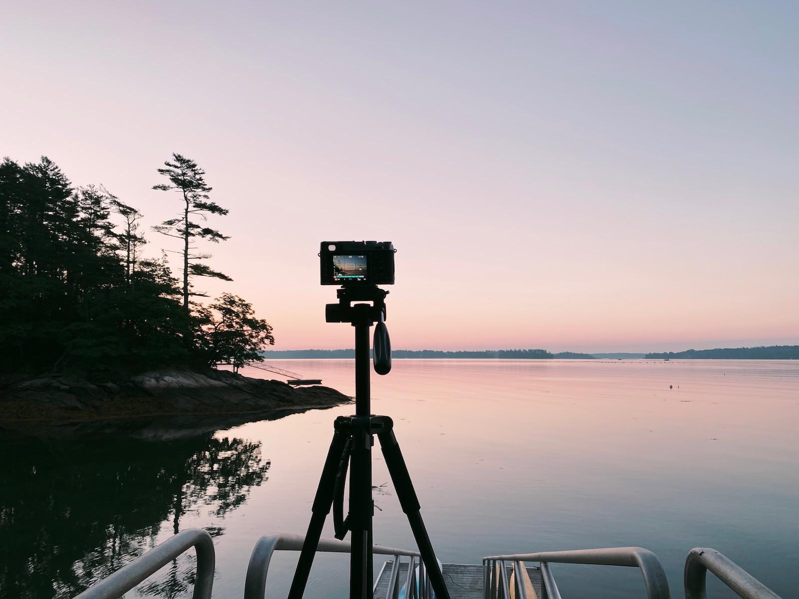 A camera mounted on a tripod with a lightening sky in the background