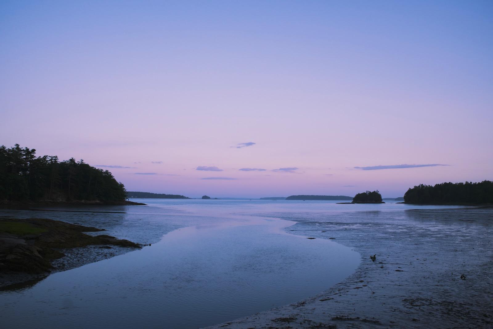 A lavender sunset sky above a coast at low tide.