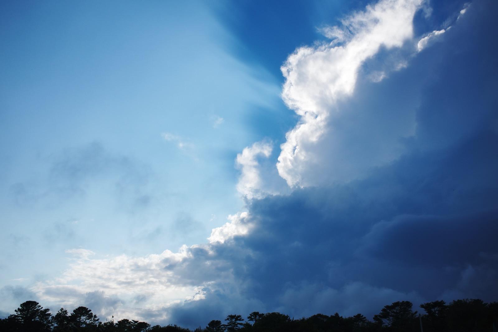 Light rays streaming through a patch of dramatic clouds against a blue sky.