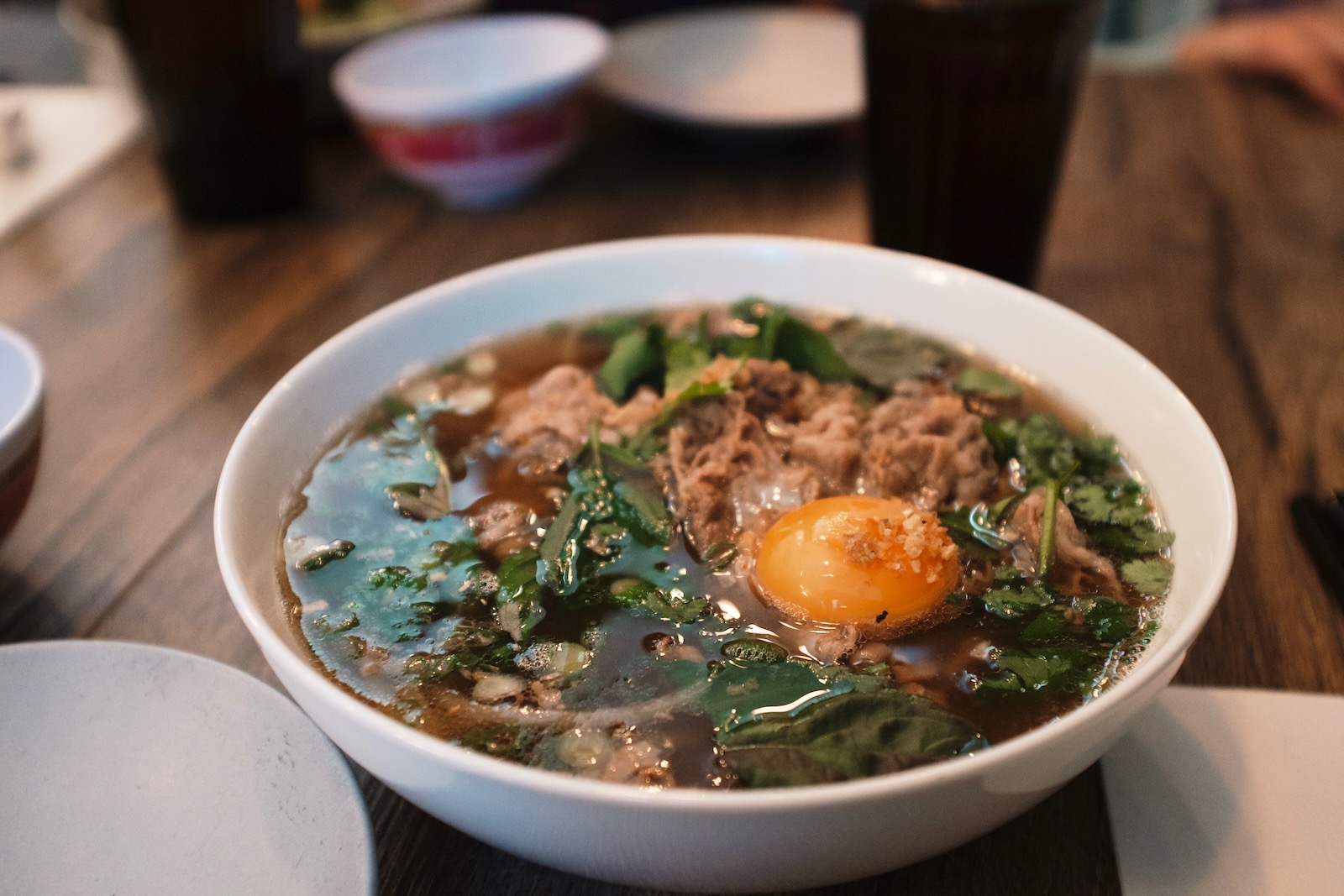 A bowl of beef noodle soup with an egg yolk delicately perched above beef and greens.