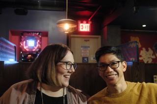A couple smile in a dimly lit sake bar.