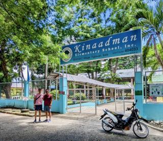 Two men stand in front of a gated entrace to an elementary school called Kinaadman.