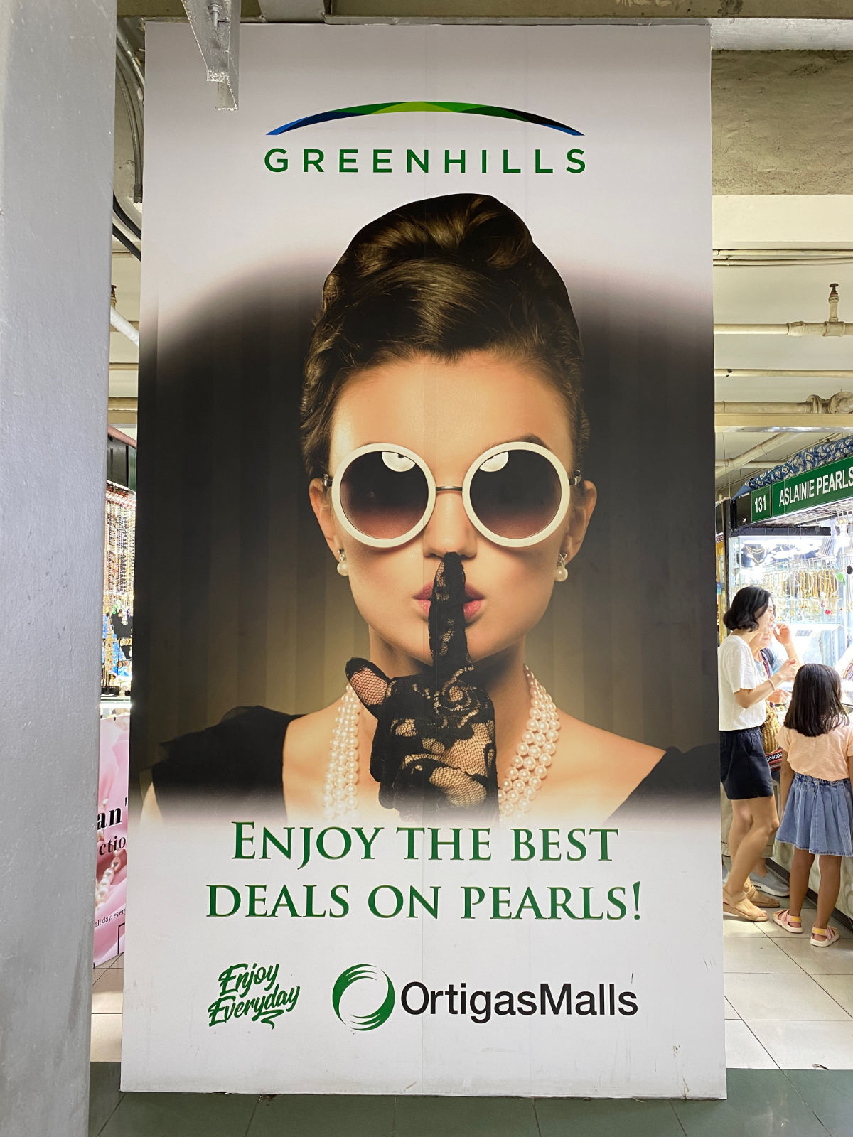 A poster: a woman made up in an approximation of Audrey Hepburn’s black-dress-and-pearls aesthetic holds her finger up to her lips.