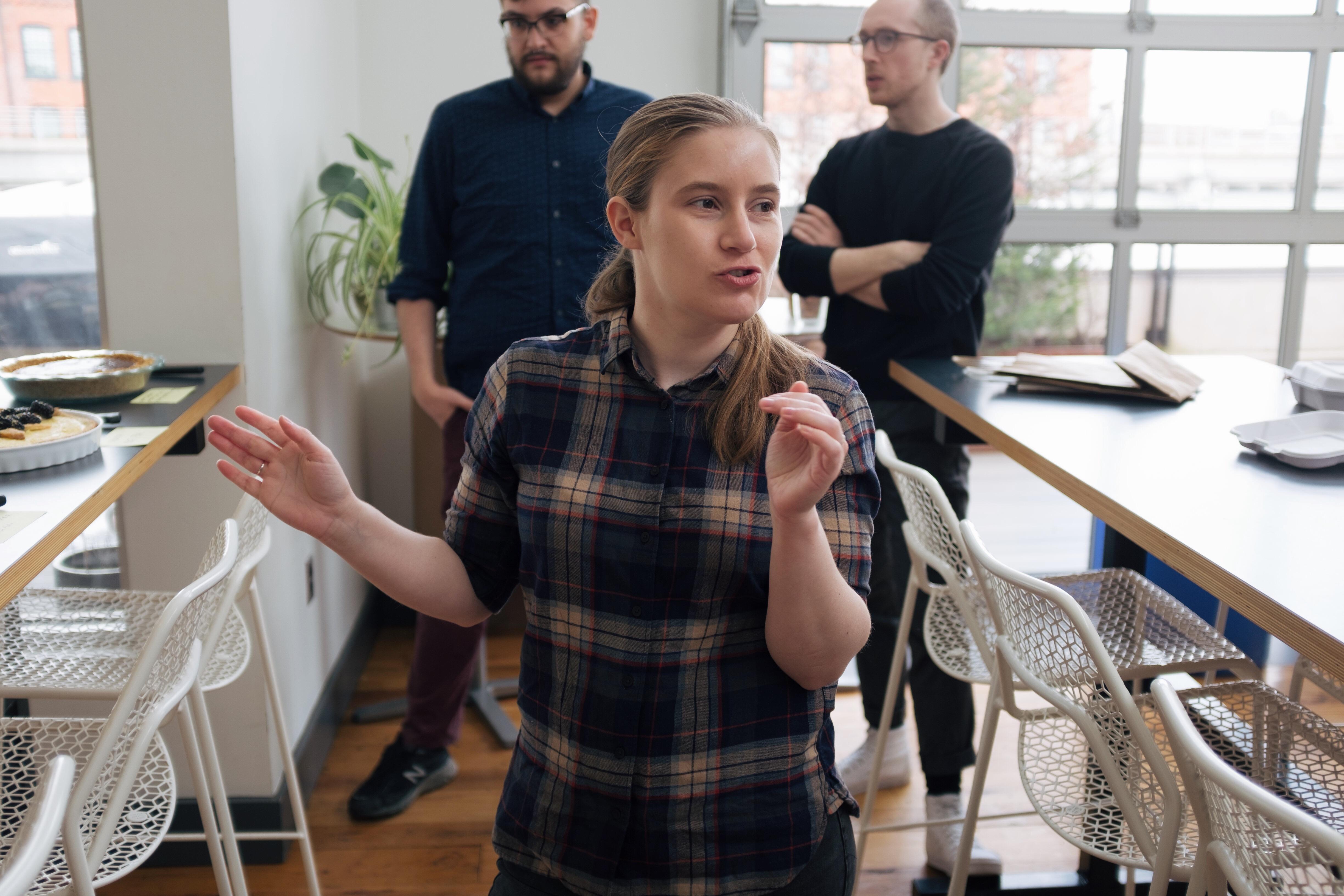 A woman between two tables explains the tasting and judging procedure.