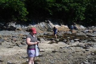 A woman holds a mesh bag of seaglass while two girls walk up the shore in the distance.