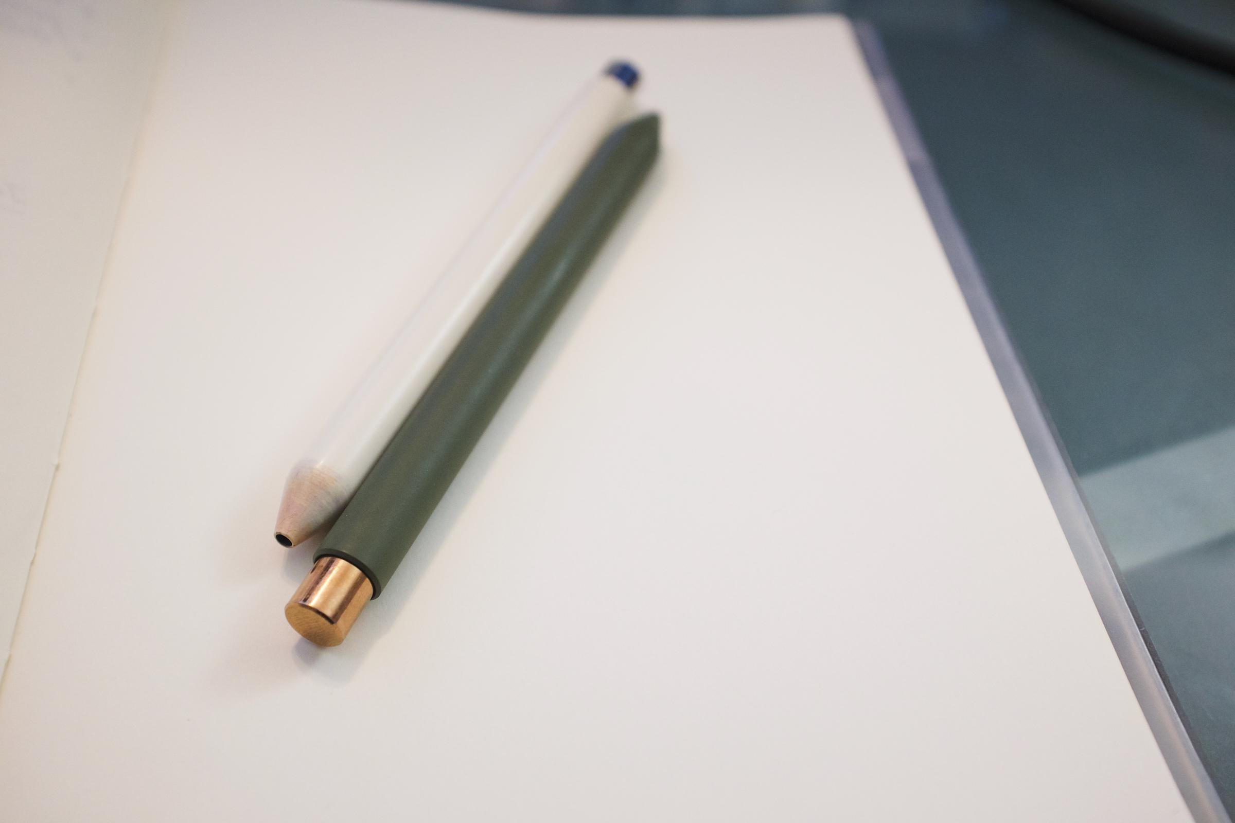 Two clicky pens side-by side: a white one with a silver clicker, and a green one with a copper clicker.