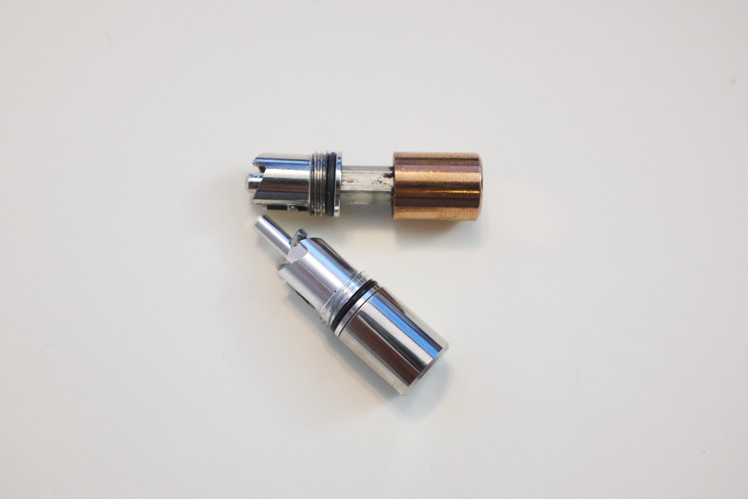 Two clicker mechanisms unscrewed from their respective pens: silver and copper.