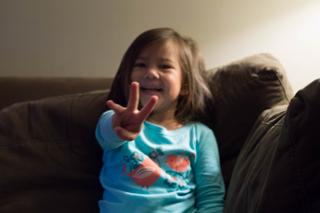 A smiling girl holds up three fingers