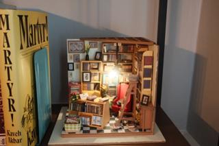 A miniature model of a study lined with bookshelves stuffed with lifelike books. A working chandelier lights up the space.