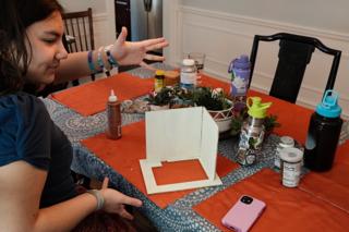 A young woman poses with a partially-assembled model’s walls.