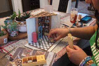A young woman puts miniature furniture into place.