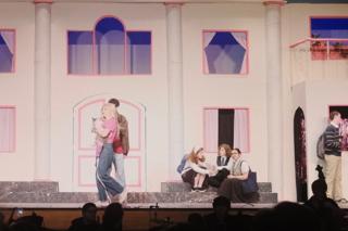 Three characters in the background of a scene from Legally Blonde The Musical.