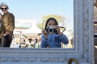 Reflection of Sophie taking a photo, while an onlooker smiles.