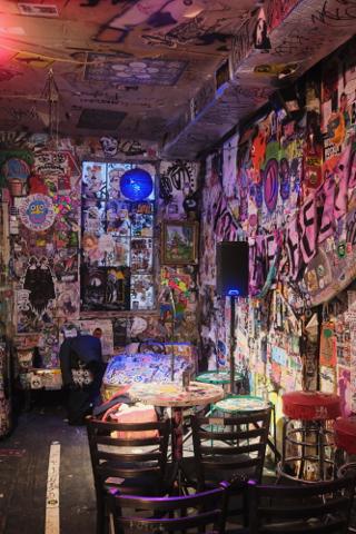 Interior space in Tattooed Mom bar, with the walls covered in stickers and flyers.