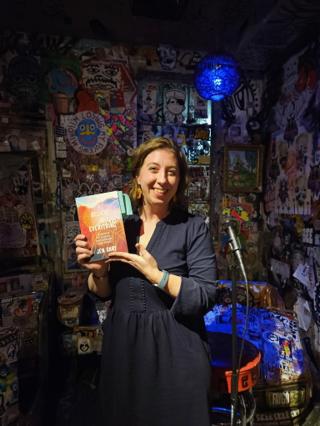 A woman holds up her book and smiles.