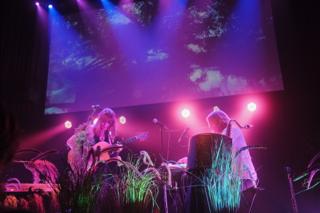 A singer plays guitar while her bandmate plays the keyboard.