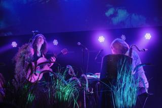 A singer plays guitar while her bandmate plays the keyboard.