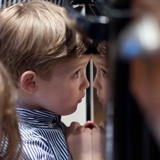 A young boy reflected in an oven door.