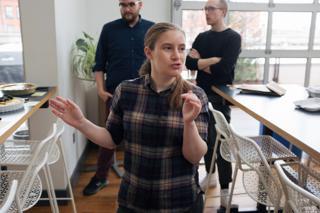 A woman between two tables explains the tasting and judging procedure.