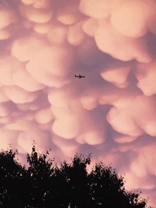 A plane silhouetted against a rapidly darkening sky, framed by little puffy clouds.