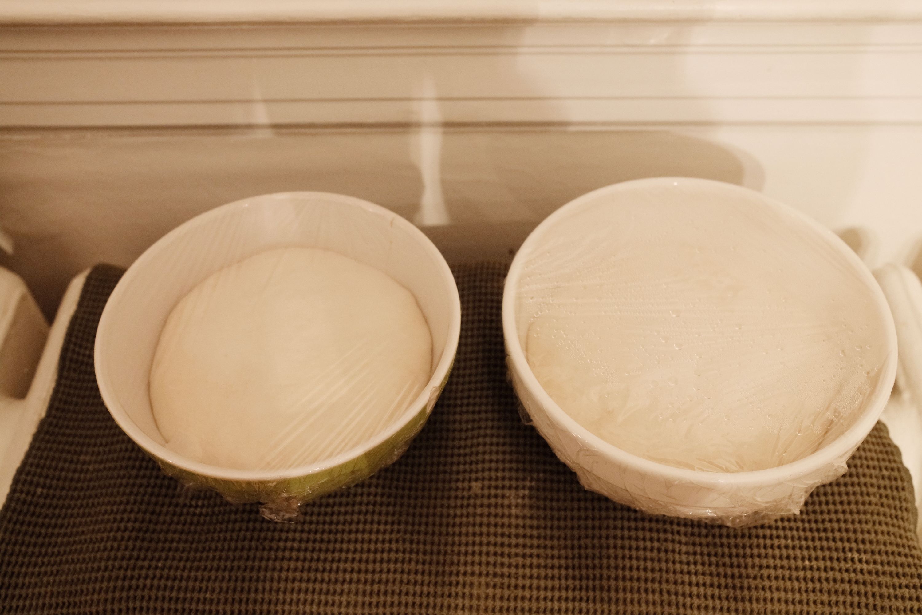 Two bowls of pizza dough left to rise atop a radiator.