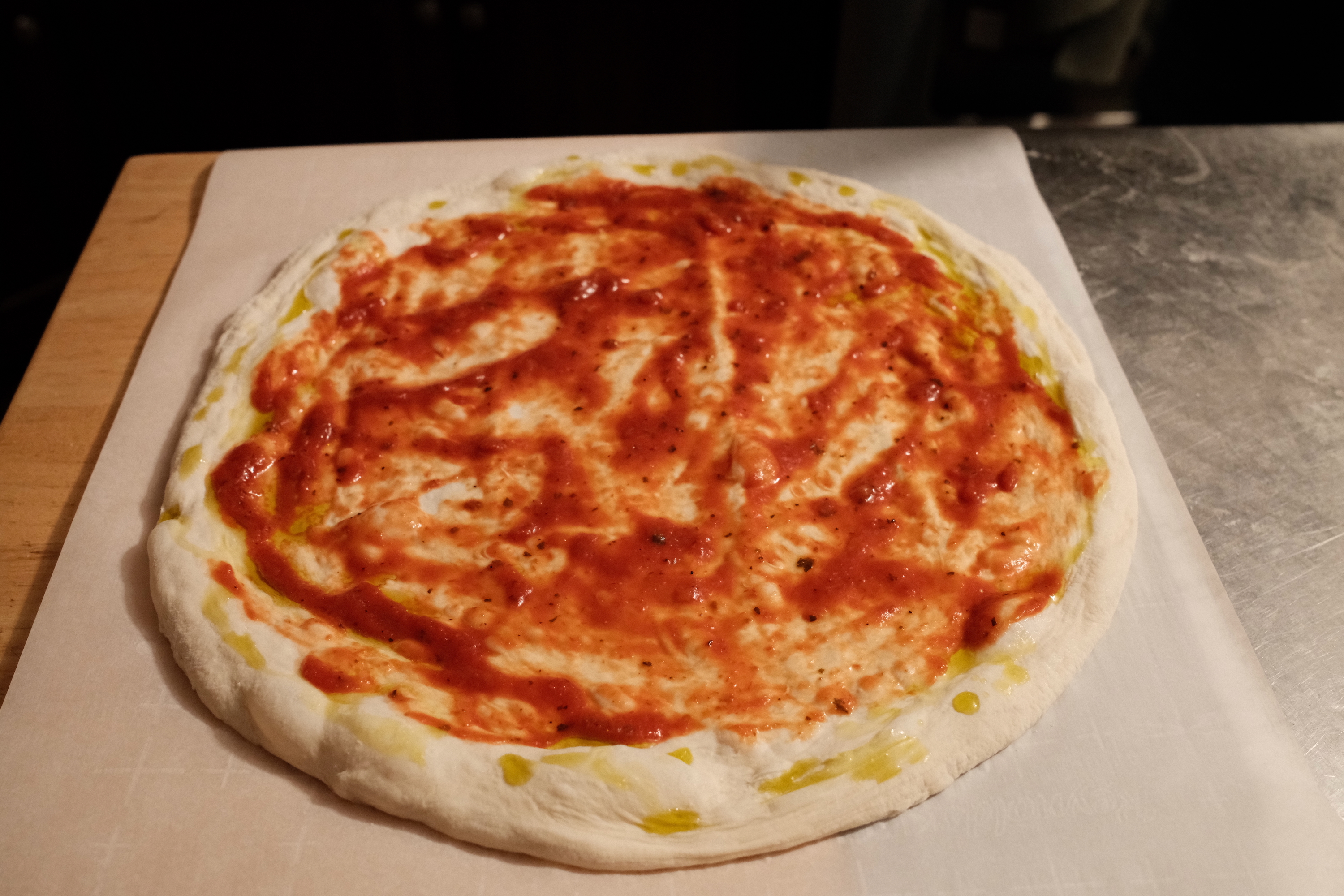Stretched dough with tomato sauce spread evenly on its surface.