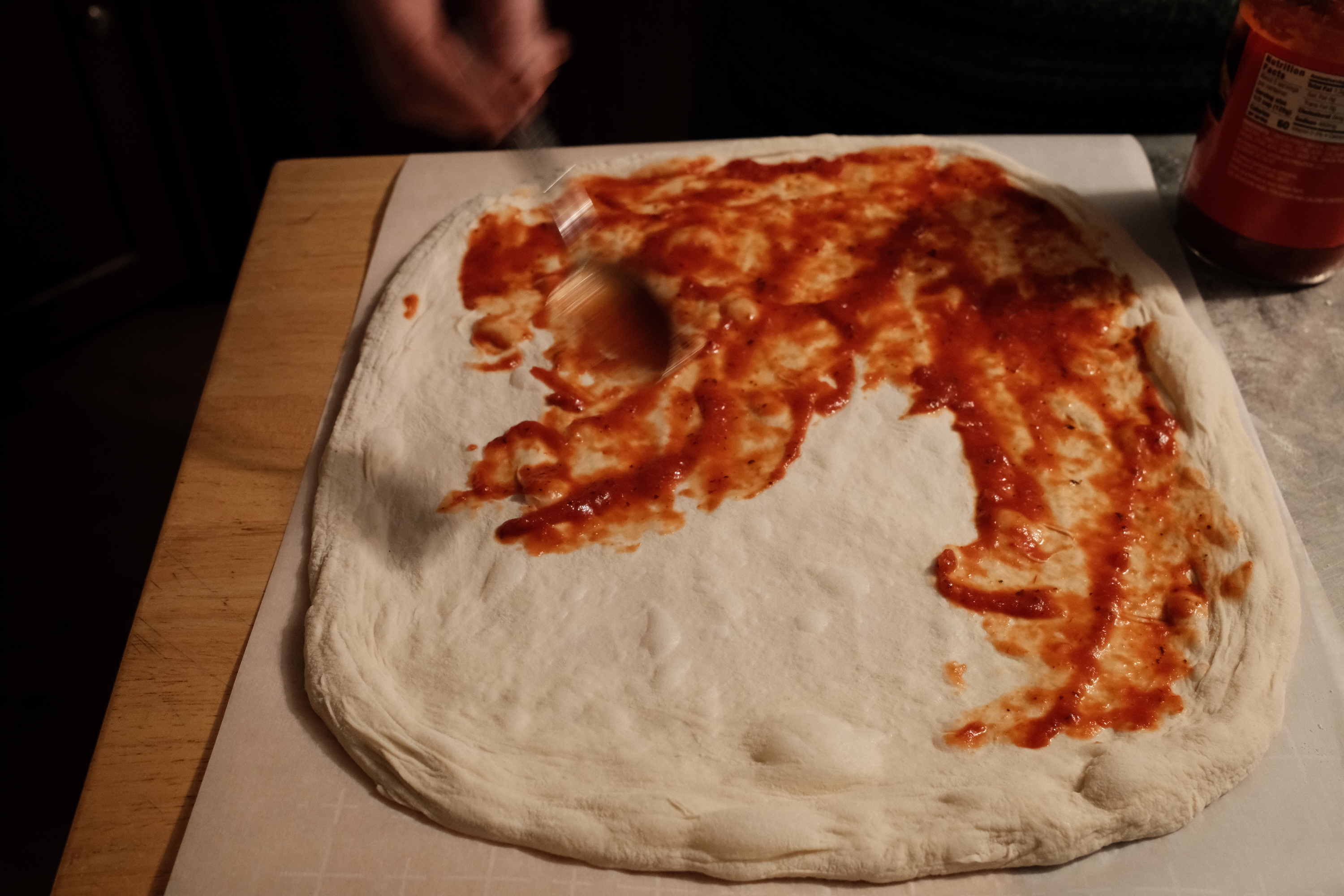 Tomato sauce being spread on stretched pizza dough.